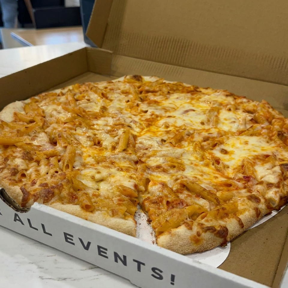 Cheesy macaroni pizza in an open cardboard box on a marble restaurant counter.