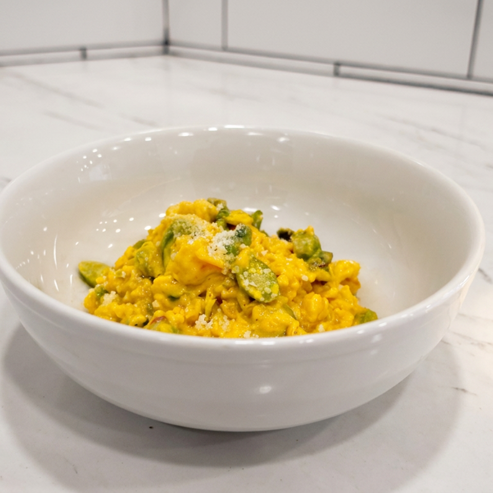 Bowl of creamy golden pasta topped with green vegetables and grated cheese on a white marble countertop.
